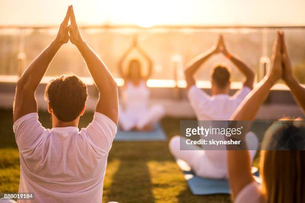 rear view of group of people doing yoga meditation exercises on a terrace. - yoga stock pictures, royalty-free photos & images