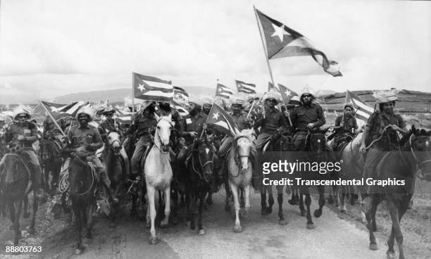 Cuban revolutionary Camilo Cienfuegos , carries the large Cuban flag on the right, while leading a group of campesinos through the coutryside as the...