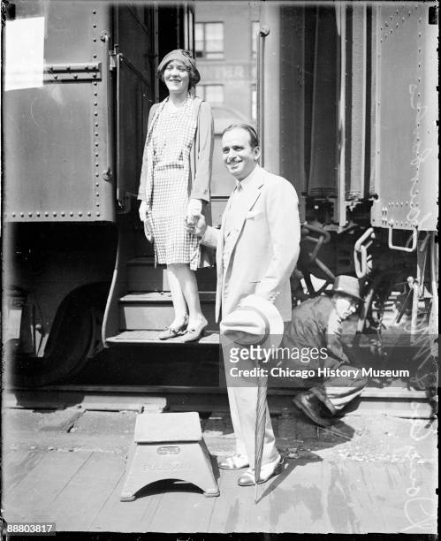 Full-length portrait of actor Douglas Fairbanks, Sr., and his wife, actress Mary Pickford, looking to the left of the camera, standing in front of a...