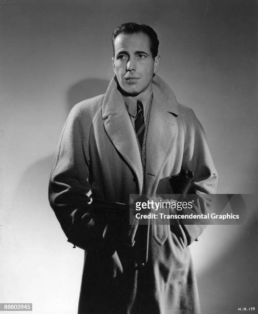Humphrey Bogart dons a trench coat during a publicity shoot in Hollywood around 1940.