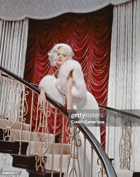 Carroll Baker poses on a grand staircase in the title role of the movie "Harlow", 1965.