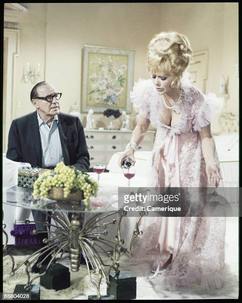 Jack Benny sits at a table while Inger Stevens pours him a glass of red wine in this scene from the movie "A Guide For The Married Man", 1967.