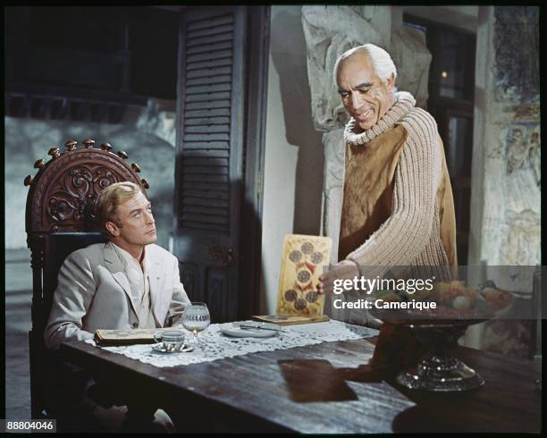 Michael Caine sits at a table while Anthony Quinn smiles and shows him a card in this scene from the movie "The Magus", 1968.