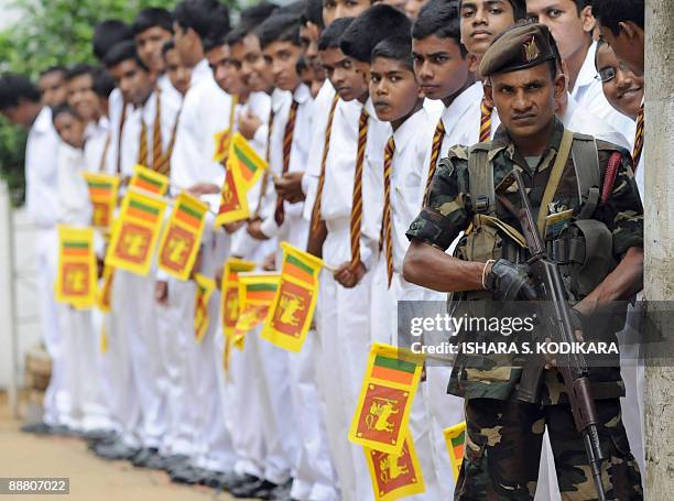 Sri Lankan soldier stands guard while school children wave the national flag during a felicitation ceremony in Colombo on July 3, 2009. President...