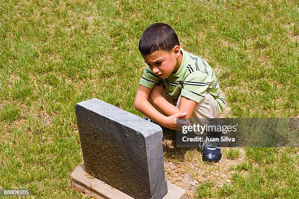 boy sitting in front of grave in cemmetery - föräldralös bildbanksfoton och bilder