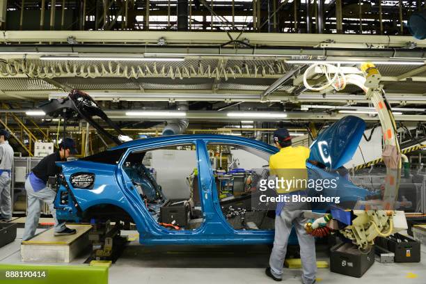 Employees work on automobile assembly on the Prius hybrid plug-in vehicle production line inside the Toyota Motor Corp. Tsutsumi plant in Toyota...