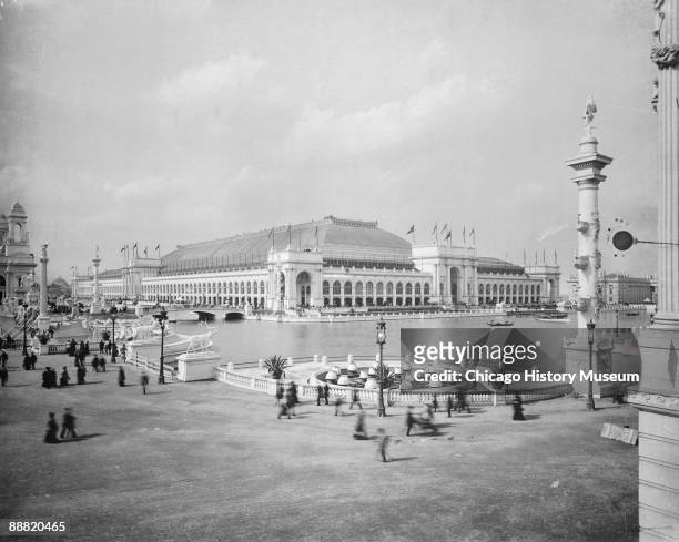View of the Manufactures and Liberal Arts Building, with people milling about on the plaza alongside the Great Basin, at the Chicago World's Fair or...
