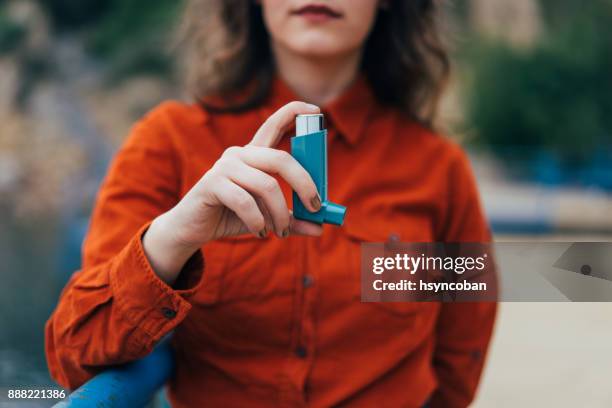 jonge vrouw met behulp van een astma-inhalator buitenshuis - asthma in adults stockfoto's en -beelden