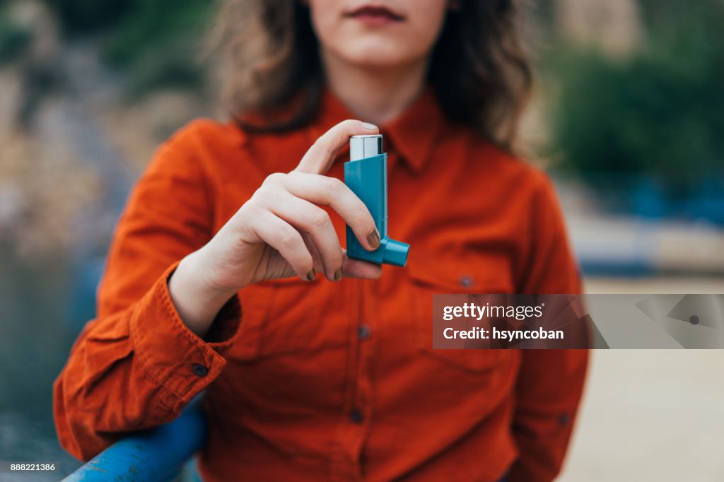 Young woman using an asthma inhaler outdoors