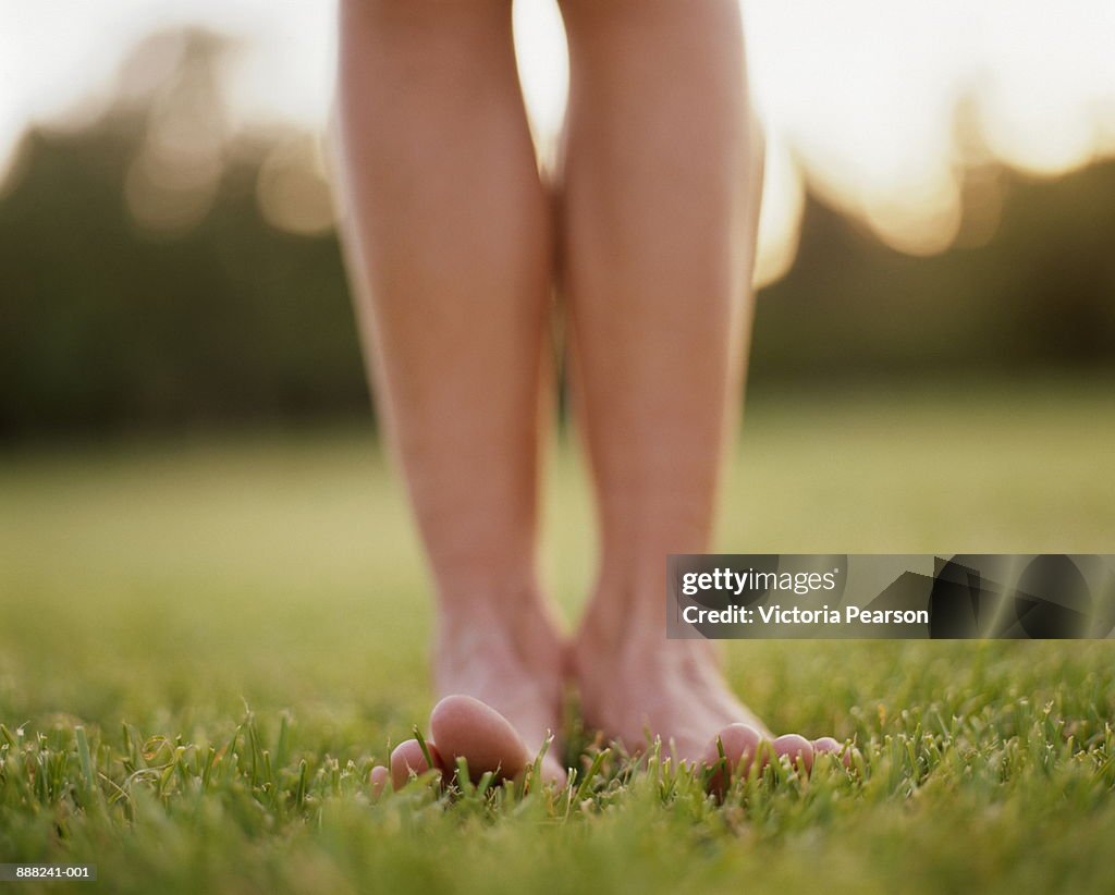 Woman standing barefoot on grass, low angle view