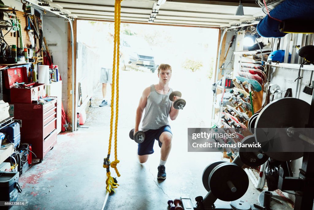 Young man doing lunges with dumbbells in gym in garage