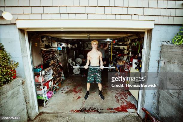young man doing curls while working out with friends in gym in garage - teen boy shorts stock-fotos und bilder