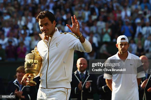 Roger Federer of Switzerland celebrates victory with the trophy as Andy Roddick of USA looks despondent after the men's singles final match on Day...