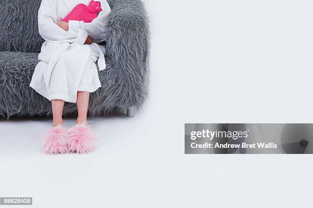 woman in bathrobe sitting on sofa holding hot water bottle - hairy woman stockfoto's en -beelden