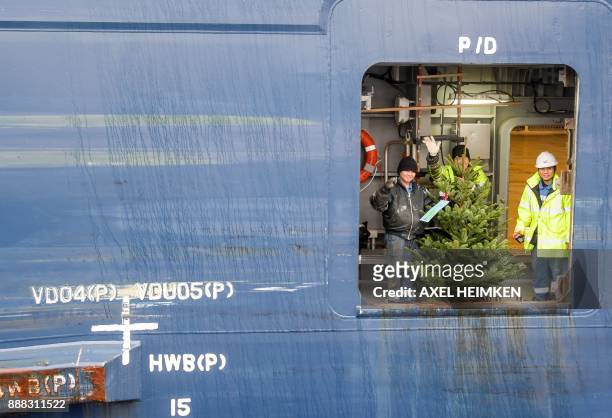 Crew members of a cargo ship wave after they received a Christmas tree at the port of Hamburg, northern Germany, on December 8, 2017. Christmas trees...