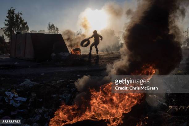 Palestinian protester pushes a tire onto a fire barricade as they clashed with Israeli border guards near an Israeli checkpoint on December 8, 2017...