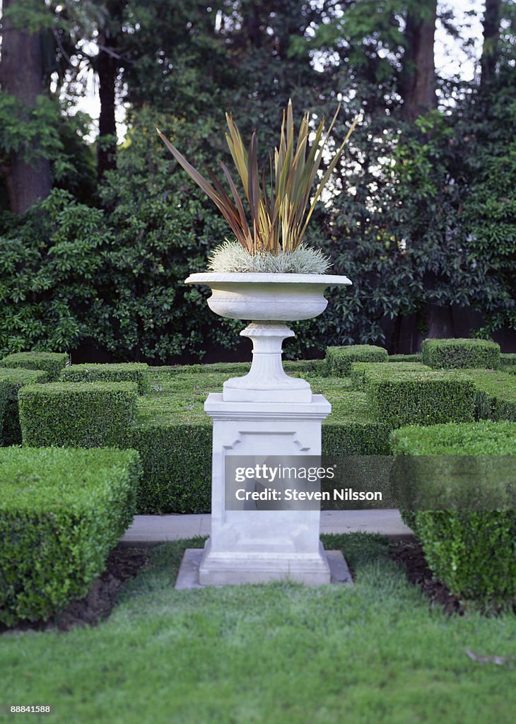Pedestal urn in garden with manicured hedges
