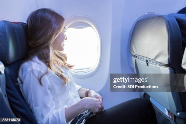 jonge vrouw kijkt uit raam van het vliegtuig tijdens de vlucht - business class seat stockfoto's en -beelden
