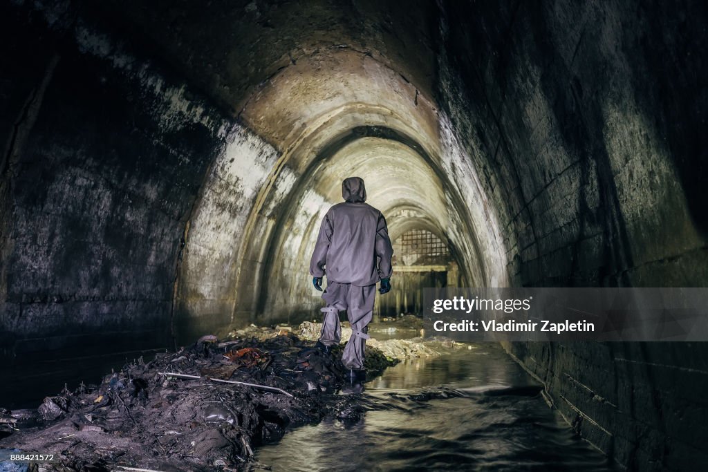 Sewer tunnel worker in chemical protective suite in underground gassy sewer tunnel