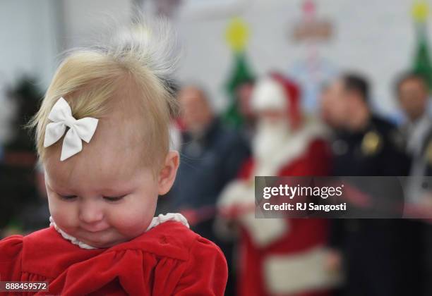 Five months-old Millie Hill is held by her mother who waits with other supporters and volunteers for Santa to cut the ribbon to start this year...