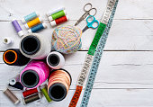 Colorful Sewing thread line spools, big and small, scissors, and measuring tape on top of a white wooden background tabletop, concept and idea