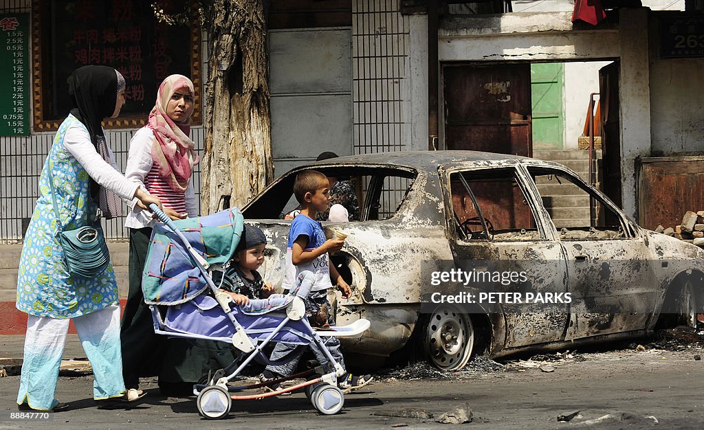 People pass a burnt out car on a street