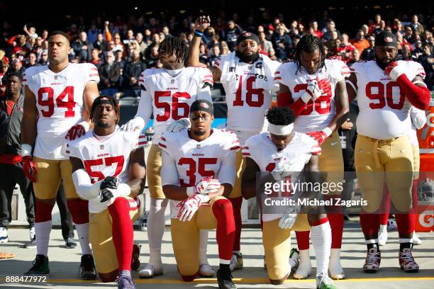 Eli Harold, Eric Reid and Marquise Goodwin of the San Francisco 49ers kneel on the sideline during the anthem as teammates Solomon Thomas, Reuben...