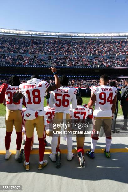 Eli Harold, Eric Reid and Marquise Goodwin of the San Francisco 49ers kneel on the sideline during the anthem as teammates Solomon Thomas, Reuben...