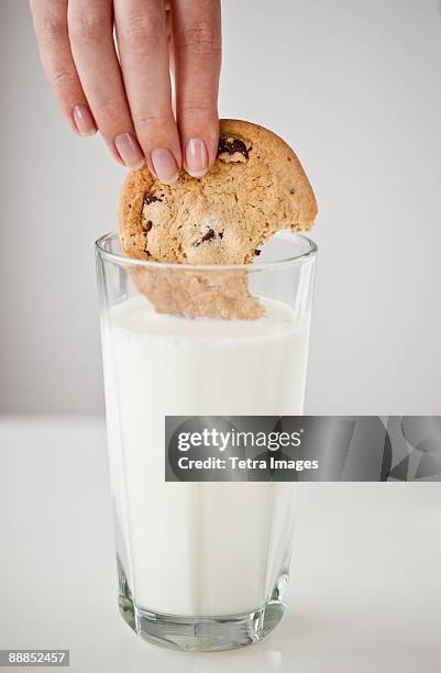 womans hand dipping cookie in glass of milk - mojar fotografías e imágenes de stock