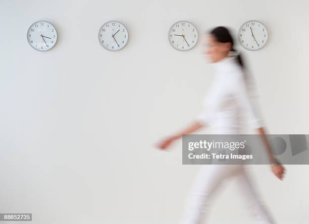 business woman walking along wall with clocks, blurred motion - one person time stock-fotos und bilder