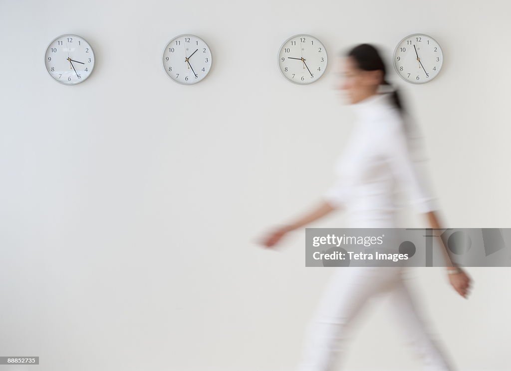 Business woman walking along wall with clocks, blurred motion
