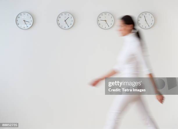 business woman walking along wall with clocks, blurred motion - one person time stock pictures, royalty-free photos & images