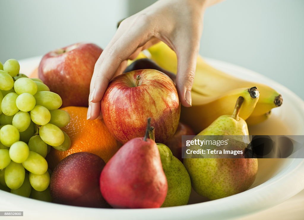 Womans hand taking apple from fruit bowl