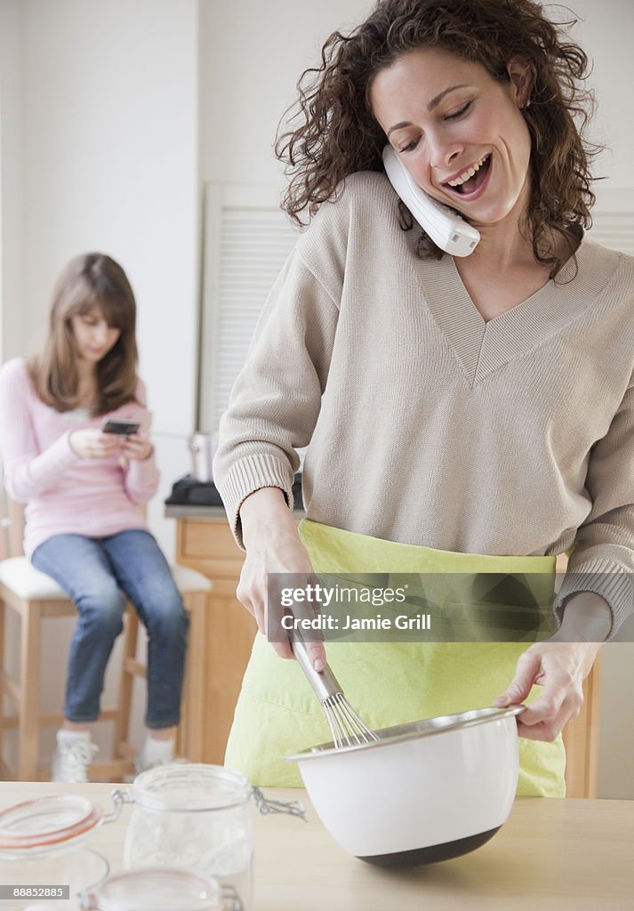 Mother preparing food while talking on the phone, daughter (10-11 years) in background