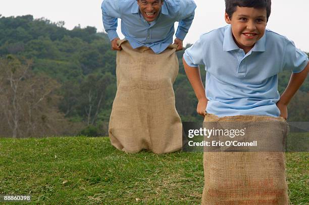 father and son jumping in potato sacks - sack race stock pictures, royalty-free photos & images