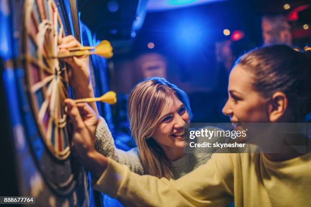 happy women talking while removing darts from dartboard. - dart stock pictures, royalty-free photos & images