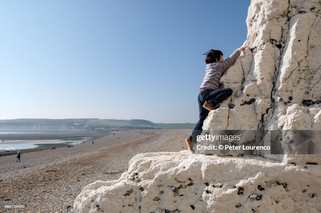 A young boy climbing up a white cliff at the beach.