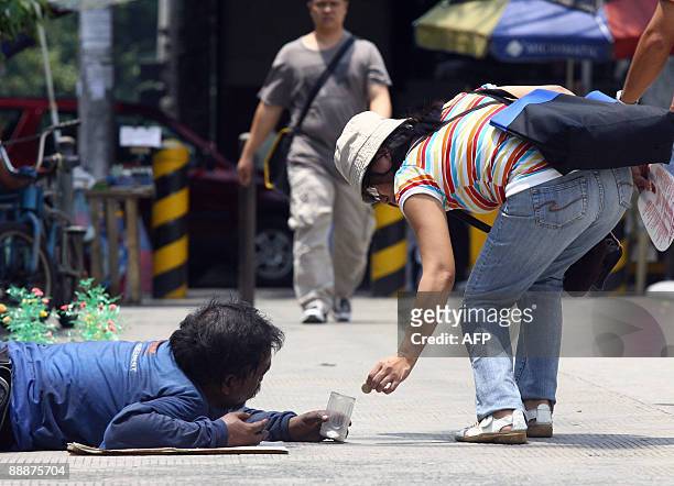 Pedestrian gives alms to a beggar along a street in Manila on July 7, 2009. Five million of the Philippines poorest families will receive cash or...