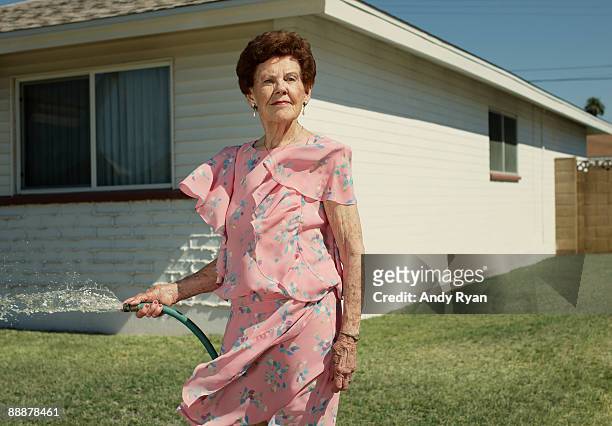 senior woman watering lawn in front of house - arizona house stock-fotos und bilder