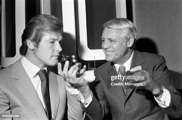 Roger Moore and Cary Grant sample one of their perfumes during their visit to their perfume company's trade show at The Inn in the Park, Park Lane,...