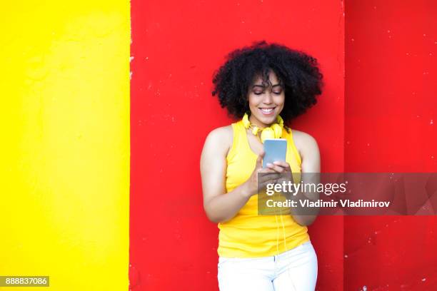 belle femme africaine avec casque jaune et téléphone intelligent - fashion pretty woman listening music in headphones with smartphone colorful photos et images de collection