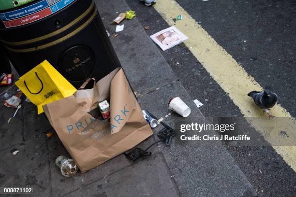 Pigeon walks past discarded Primark and Selfridges shopping bags next to a rubbish bin on Oxford Street on December 9, 2017 in London, England. With...