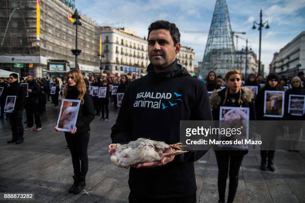 An activist of pro-animal rights group 'Igualdad Animal' holds a dead chicken while others hold pictures of mistreated animals during a protest for...