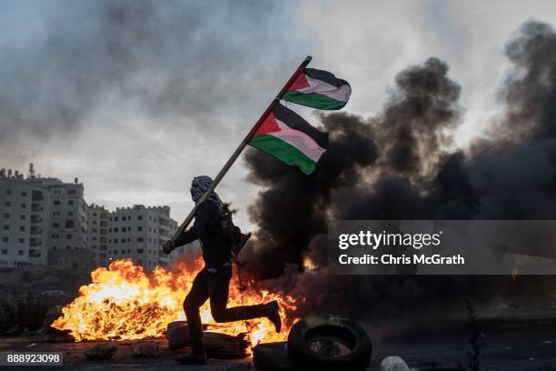 Palestinian protester runs past a burning barricade carrying a Palestinian flag during clashes with Israeli border guards near an Israeli checkpoint...