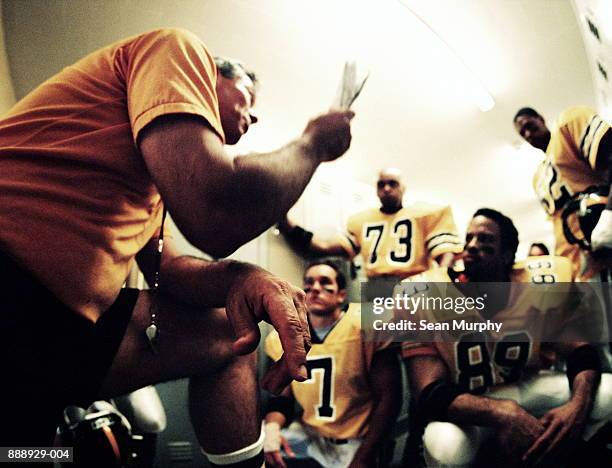 american football coach giving players pep talk in locker room - american football coach stock-fotos und bilder