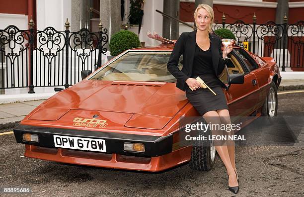 Woman stands next to the 1980 Lotus Turbo Esprit from the James Bond film "For Your Eyes Only" holding a limited edition replica pistol from "The Man...