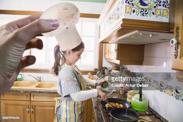 original picture of girl cooking at home doing the mother role in kitchen with funny moment using mushroom like chef hat playing with perspective from photographer perspective. - children funny moments stock pictures, royalty-free photos & images