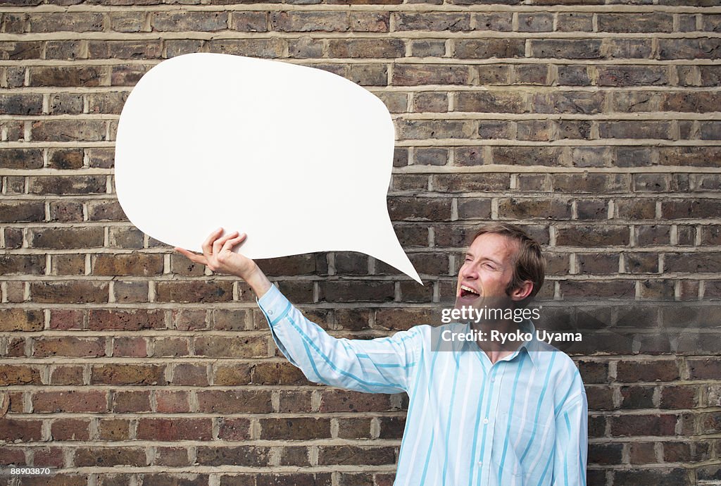 Man holding speech bubble beside brick wall