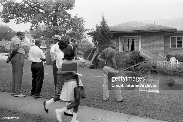 Group of onlookers stand on a sidewalk in front of NAACP attorney Arthur Shores' bomb-damaged home, Birmingham, Alabama, September 5, 1963. A sign on...