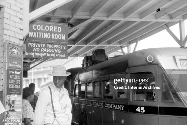 View of a passengers under a sign that reads 'Colored Waiting Room' at a bus station , Durham, North Carolina, 1940. Several buses, one from the...